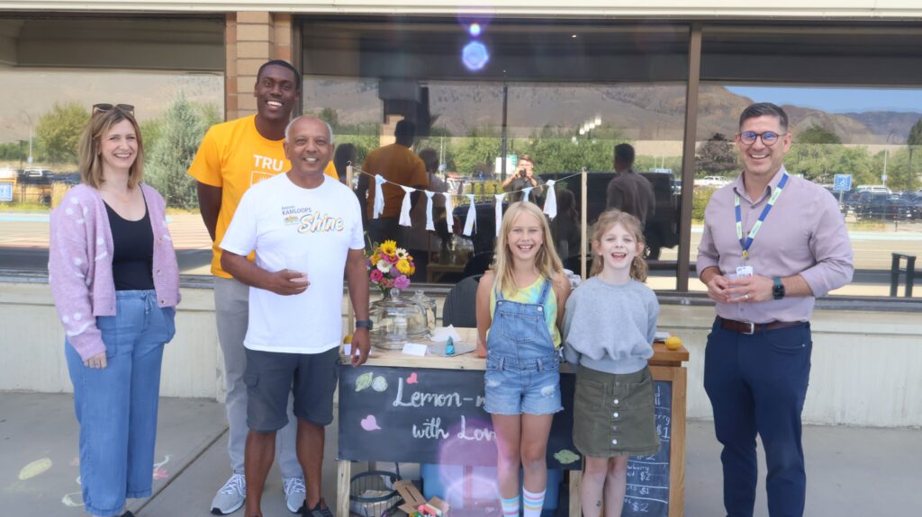 Bill Sarai of the of Kamloops Airport Authority Society and Jim Moroz of Kamloops Airport Limited standing with the lemonade stand and it's young operators.